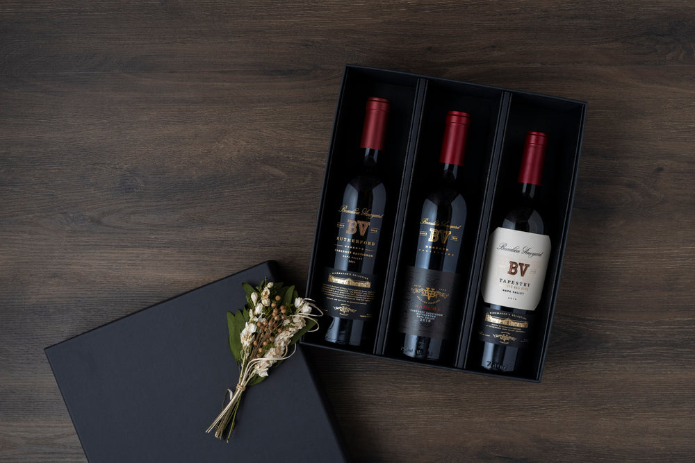 Three bottles of BV wine in a black box on a wooden surface