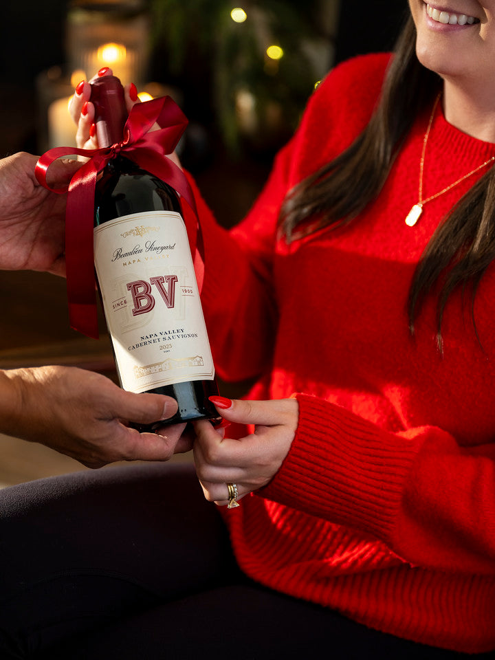 A woman receiving a bottle of Beaulieu Vineyard Cabernet with a bow on it.