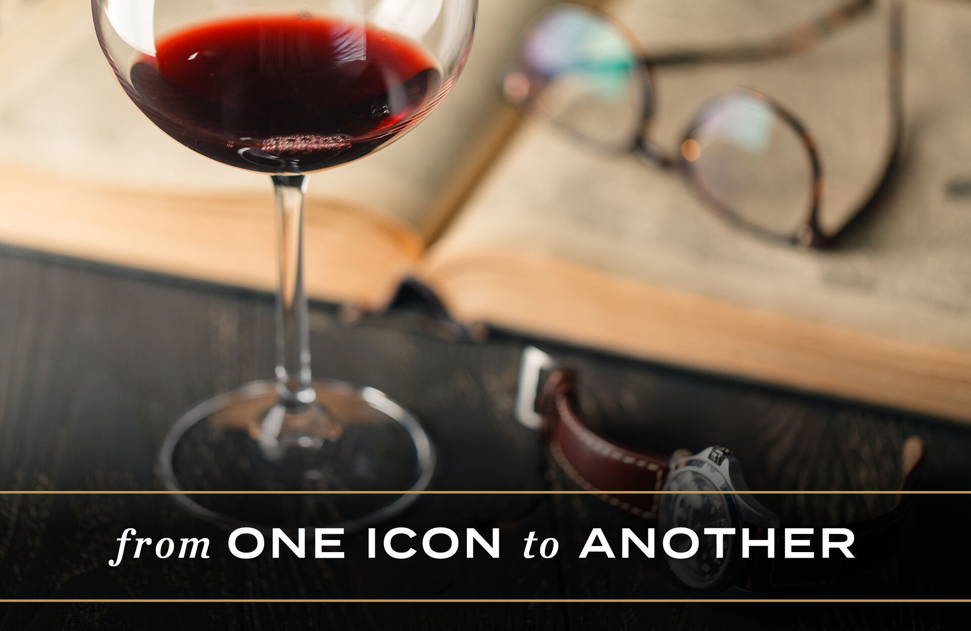 Glass of wine on a desk with glasses and a watch.